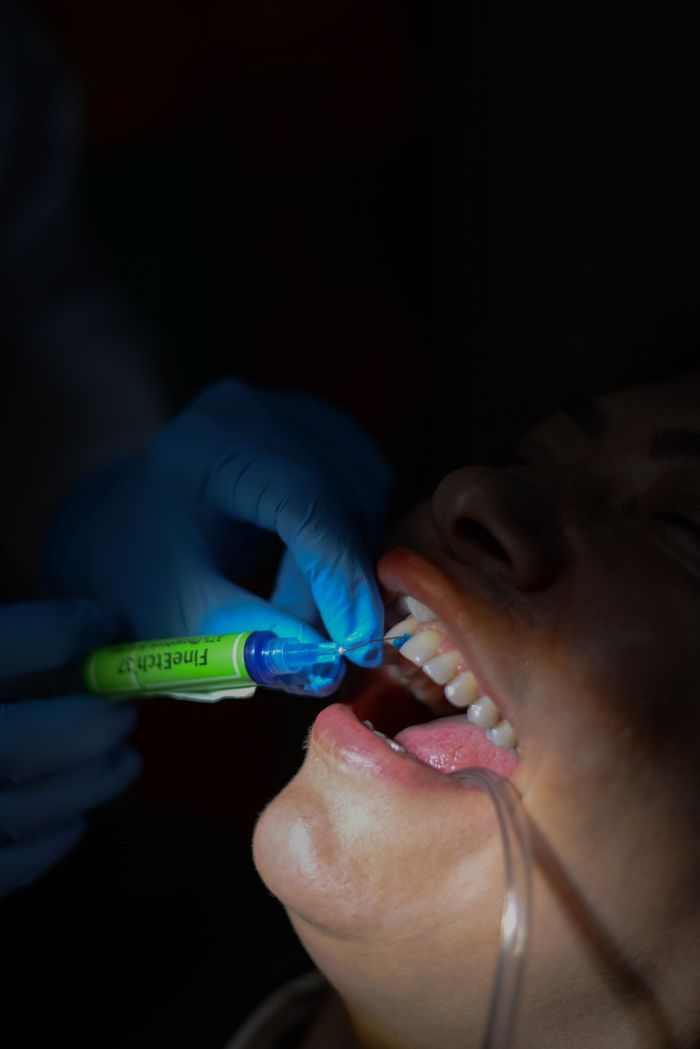 services-04 A dentist holds a syringe near a patient's mouth under dim lighting, showcasing precision dental care.