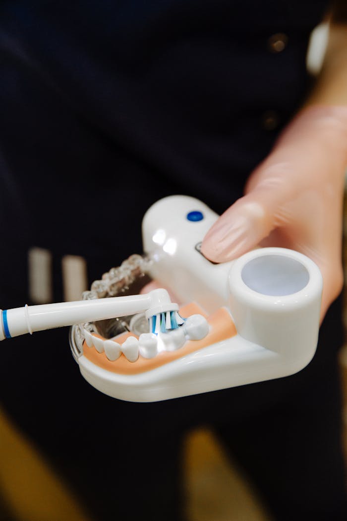 services-img Crop unrecognizable woman wearing uniform in latex gloves using electric brush to apply toothpaste on jaw mockup for everyday teeth treatment procedure